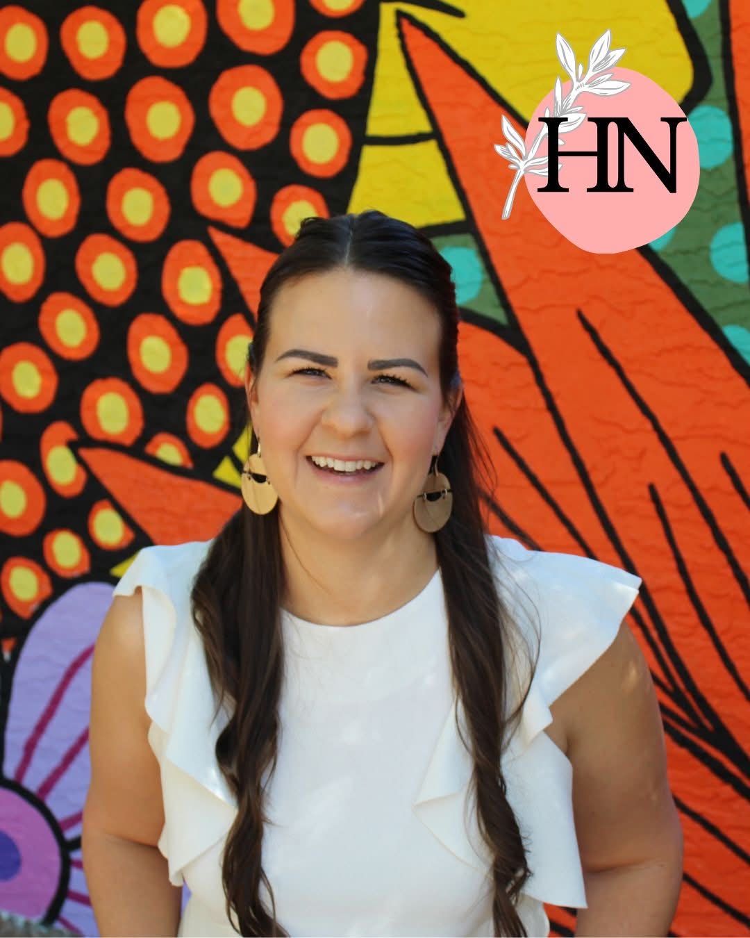 Paula Hardy smiling in a white ruffled top against a vibrant orange, yellow, teal, and purple mural, with The Hardy Nutritionist's pink circular logo badge in the corner.