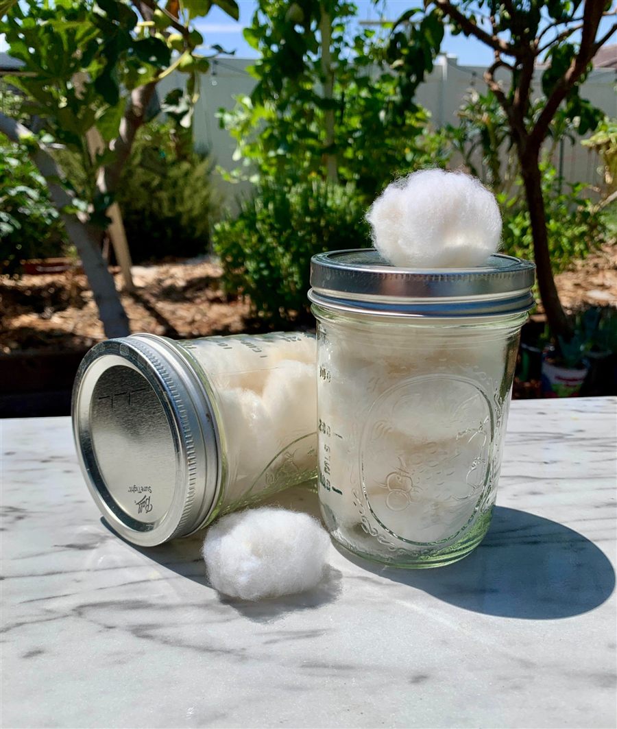 Two glass jars of handmade organic cotton balls, one open, one tipped on its side.
