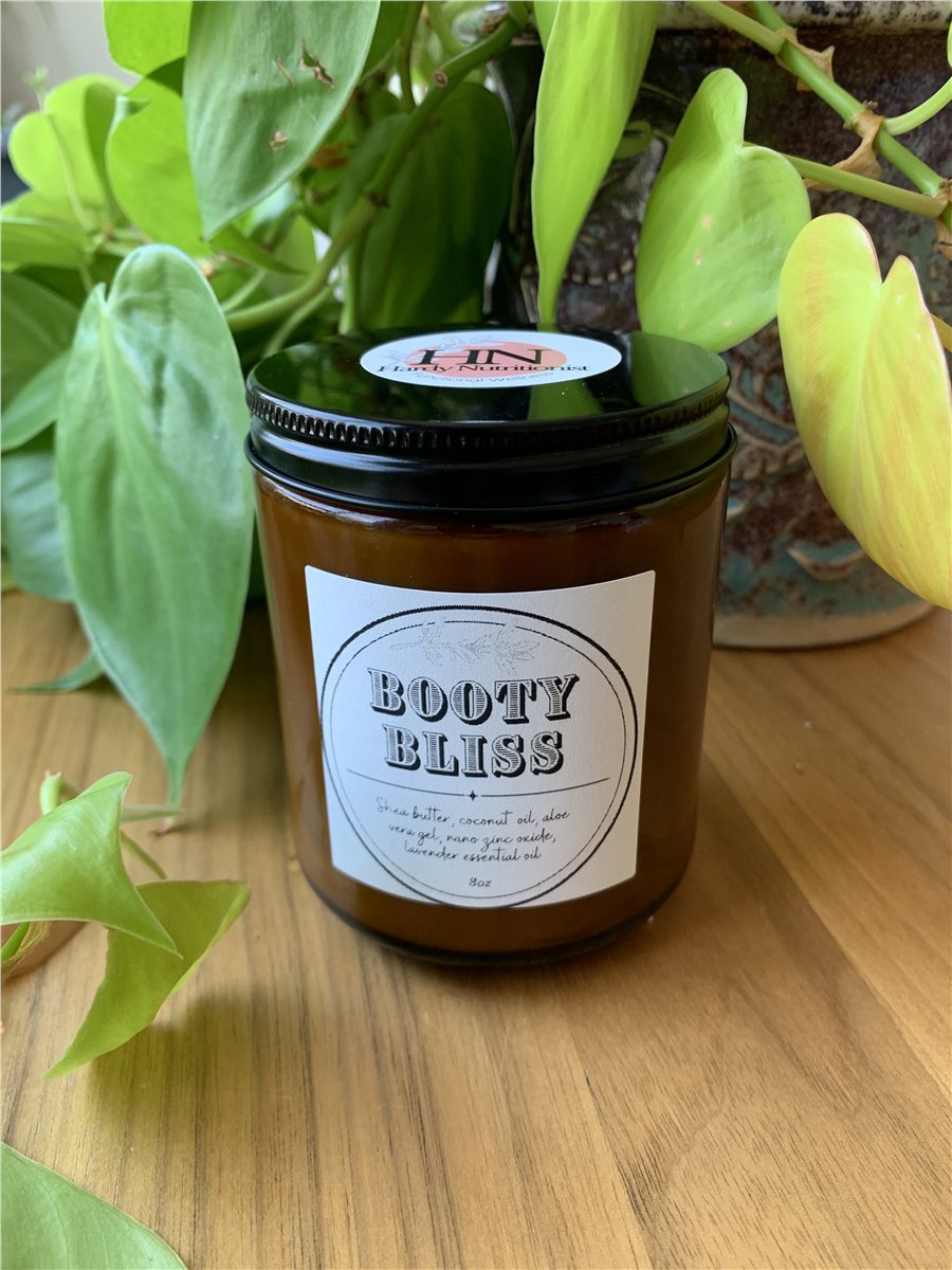 A jar of Booty Bliss diaper cream, labeled, on a wood surface.